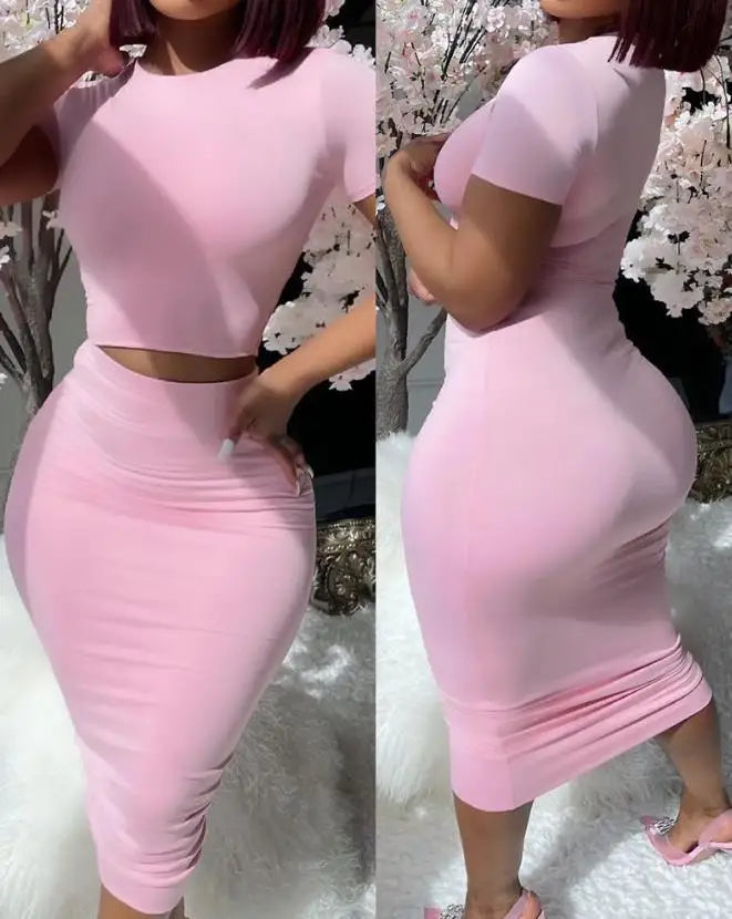Duas visões lado a lado de uma pessoa vestindo o elegante Selluve Conjuntos de Duas Peças para Mulheres em rosa claro, com um top curto de manga curta e saia lápis na altura do joelho. Elas estão perto de flores rosa claro, banhadas por uma iluminação natural suave, incorporando sofisticação e sensualidade.