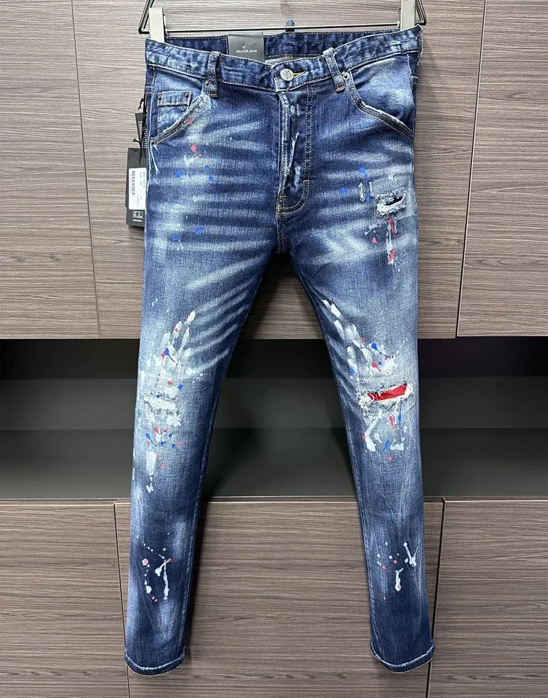 Jeans Selluve DSQ2 Denim azul desgastado pendurado contra um fundo de madeira. Esses jeans premium, slim-fit, apresentam rasgos e áreas desbotadas, acentuados com respingos de tinta branca, azul e vermelha para um visual ousado.