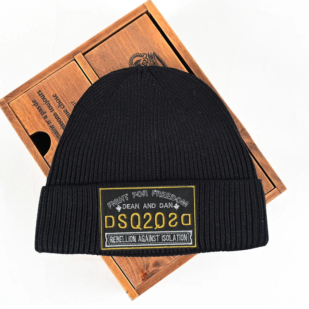Um gorro preto de malha Selluve n para mulheres repousa sobre uma caixa de madeira, apresentando um remendo bordado de alta qualidade com Luta pela Liberdade. Dean e Dan. DSQ2020. Rebelião Contra o Isolamento em amarelo e branco ousados, prometendo um inverno quente e cheio de estilo.