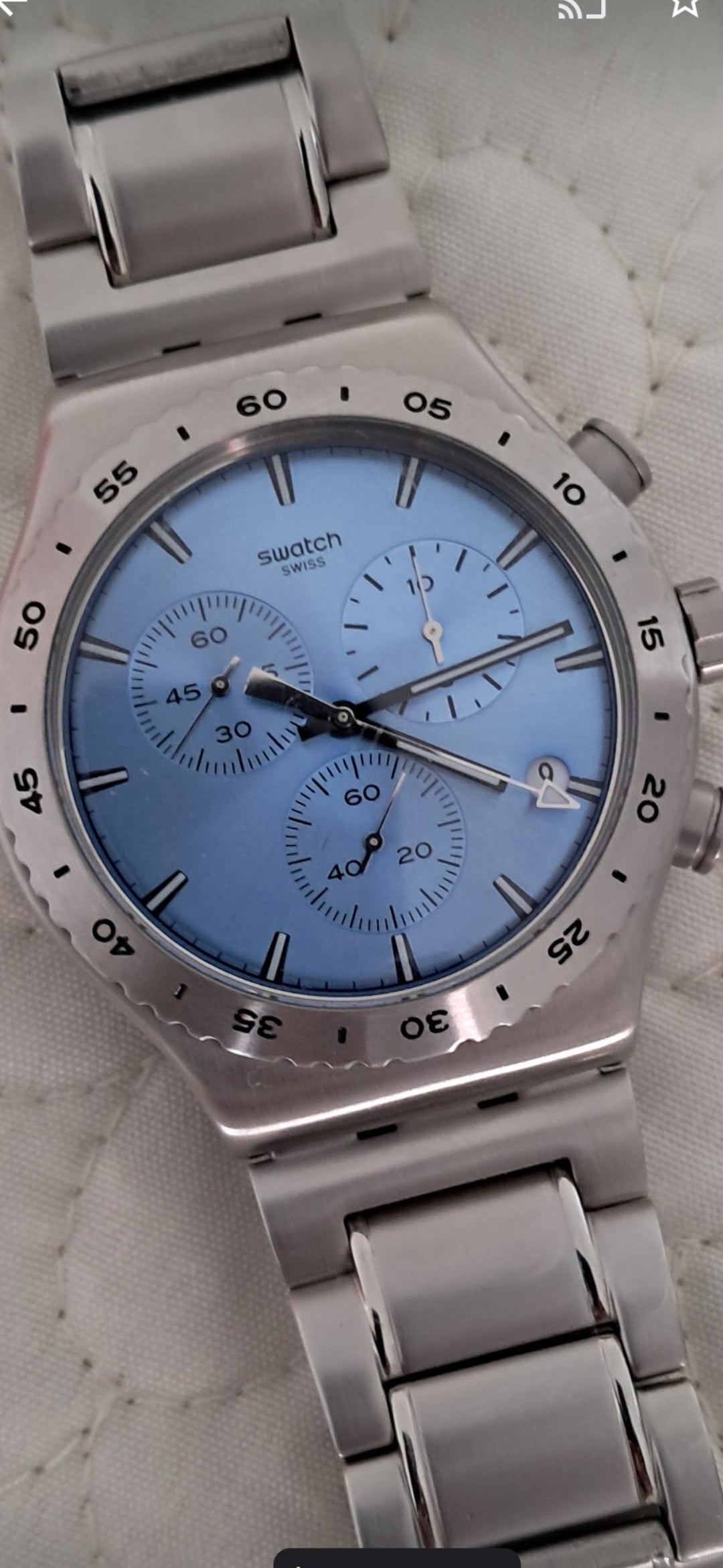 O Relogio de luxo da Selluve é um relógio de pulso prateado com pulseira de metal e mostrador azul, com indicadores de minutos ao redor do aro, três submostradores para funções de cronômetro e uma janela de data.